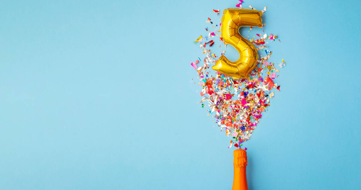 A gold balloon shaped like the number 5 with colorful confetti exploding from an orange bottle on a light blue background.