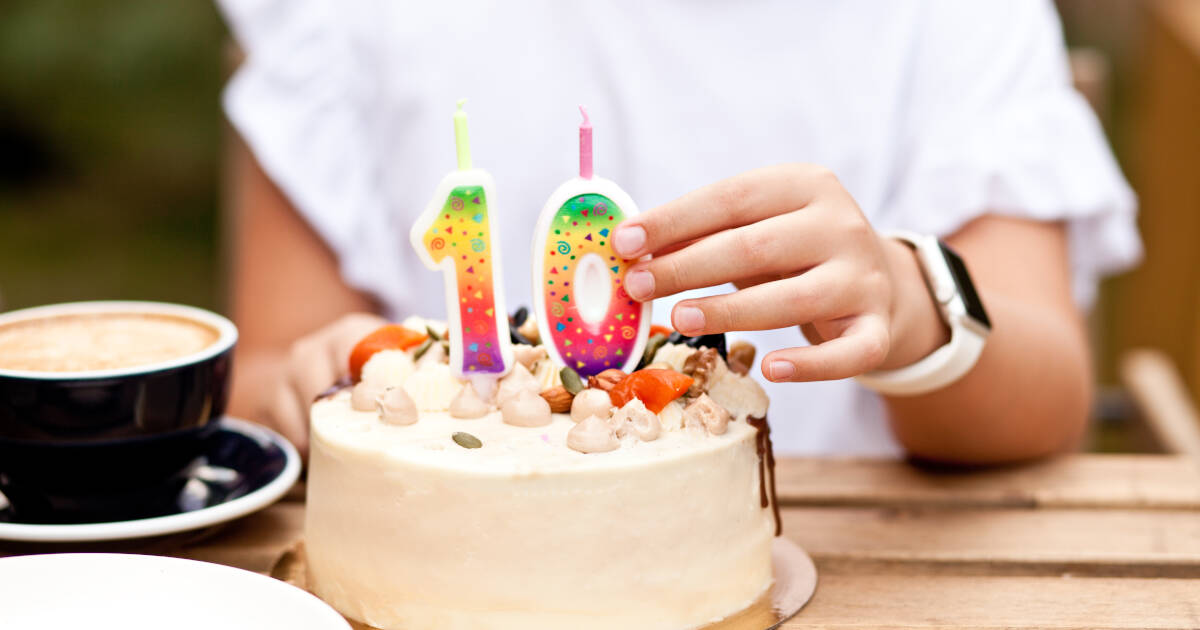 Child placing colorful number 10 candles on a birthday cake with frosting and nuts, with a cup of coffee on the table beside them.