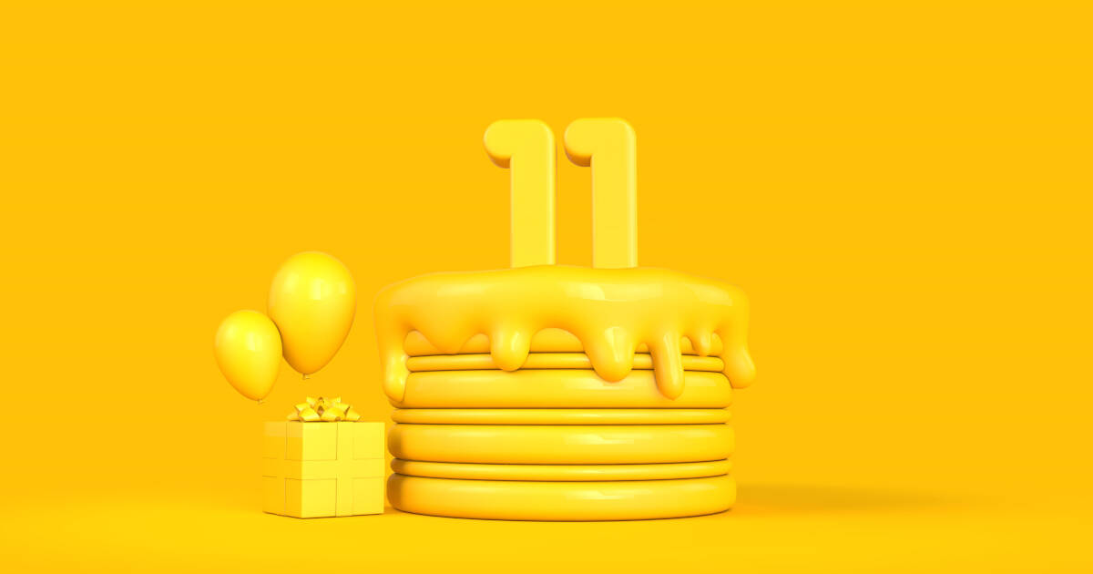 Yellow cake with number 11 candles, three balloons, and a gift box on a slid yellow background.