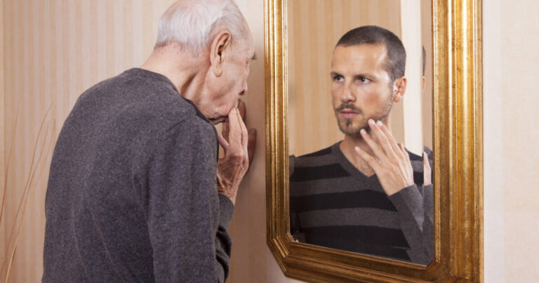 Elder man looking at a younger himself in the mirror.