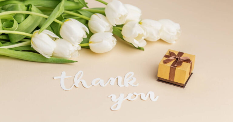 Display Of Gratitude Featuring White Tulips, and a Tasteful Gift Box With a red ribbon.