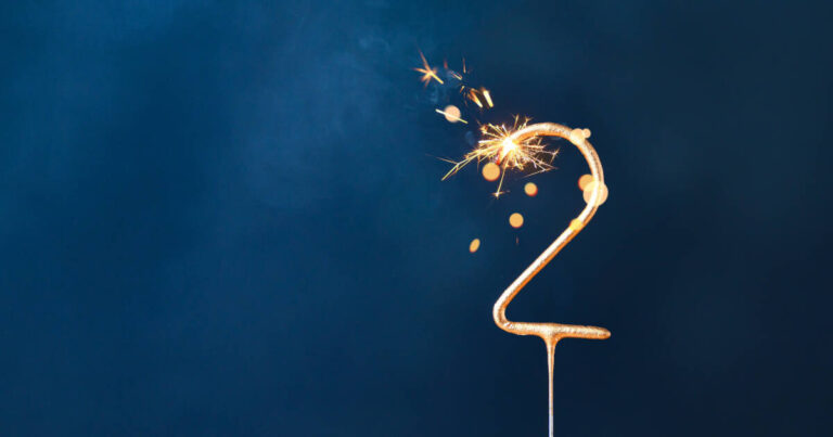 A number 2 shaped sparkling candle lit against a navy background.