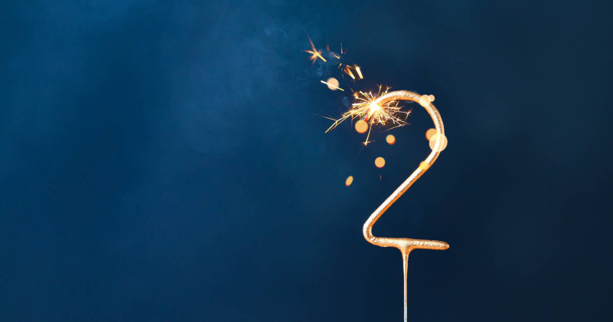 A number 2 shaped sparkling candle lit against a navy background.