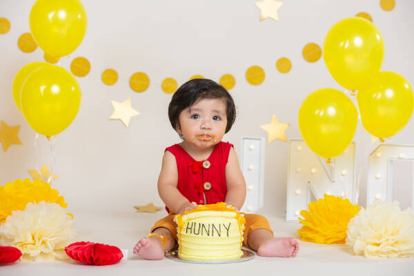 1-year-old boy celebrates his first birthday with a humorous 'HUNNY' smash cake and yellow balloons in the background.