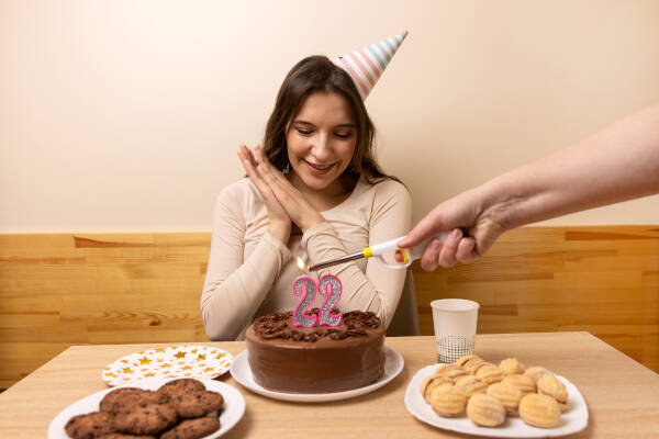 22-year-old girl sits with a cake adorned with '22' candles, being lit by a hand from off-screen