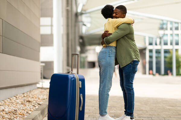 A couple embraces outside an airport terminal, their luggage beside them, as they share a farewell or reunion moment.