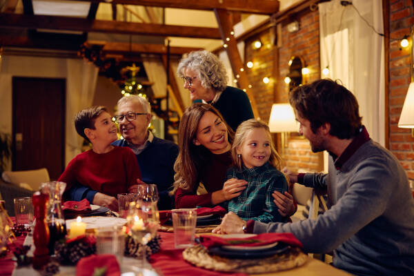 A family enjoying a warm holiday dinner together in a cozy home decorated with string lights and festive decor.