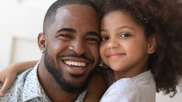 A father and daughter smiling warmly as they pose together, close-up shot of their faces.