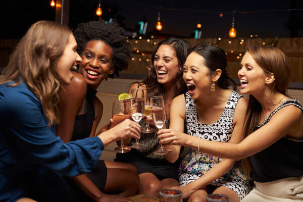 A group of female friends enjoying a night out at a rooftop bar, raising their glasses in a toast and laughing together.