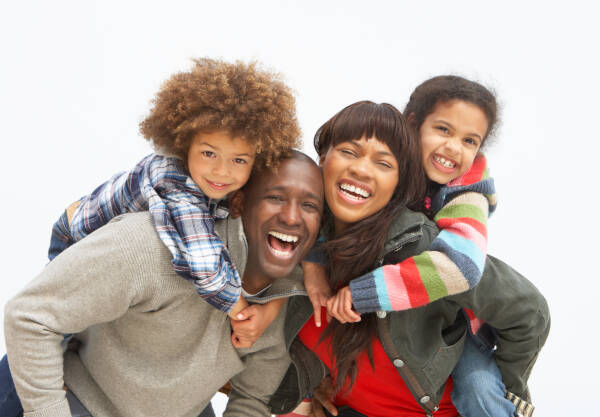 A joyful family portrait with two parents and two children, laughing and hugging each other closely in front of a white background.