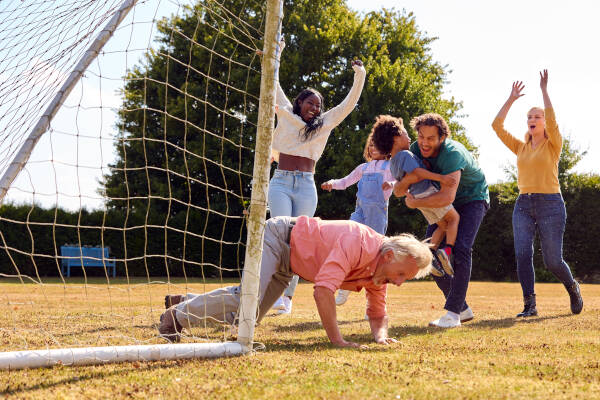 A multigenerational family playing soccer in a yard, celebrating a goal with laughter and excitement.