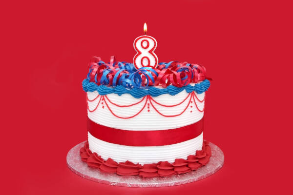 A patriotic-themed birthday cake with red, white, and blue frosting, topped with a number eight candle on a bright red background.