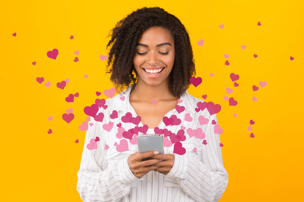 A woman smiles while using her phone, surrounded by pink heart graphics, against a bright yellow background.