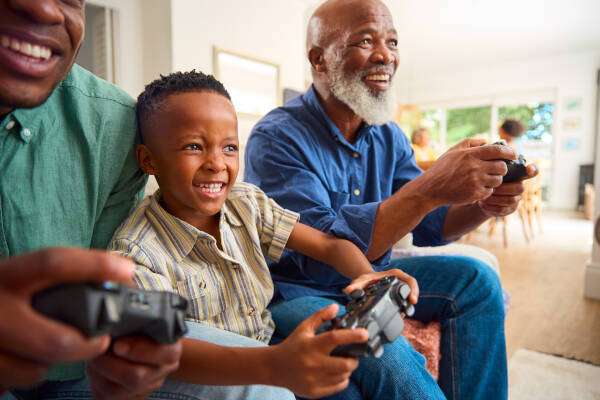 A young boy smiles as he plays video games with two older men, all holding controllers and enjoying the moment together.