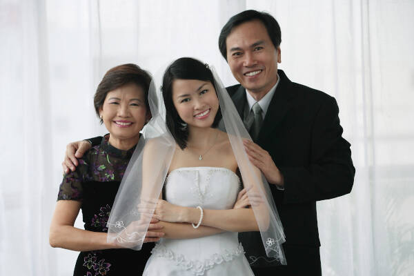 Aunt and uncle stand behind niece with arms around each other, smiling.