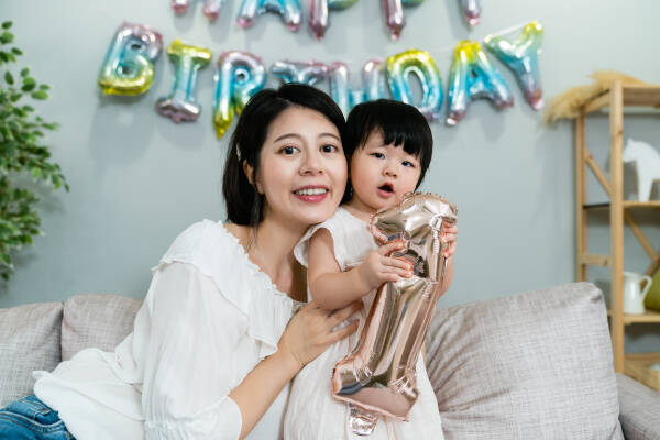 Baby girl looks at the camera, holding a number 1 standee, with her happy mother leaning close.