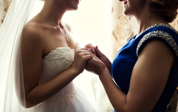 Close-up of a bride in her wedding dress, gently holding her aunt's hands on her wedding day.