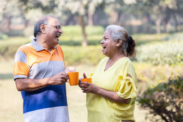  Elderly couple laughing together outdoors, holding orange mugs while enjoying each other's company in a park.