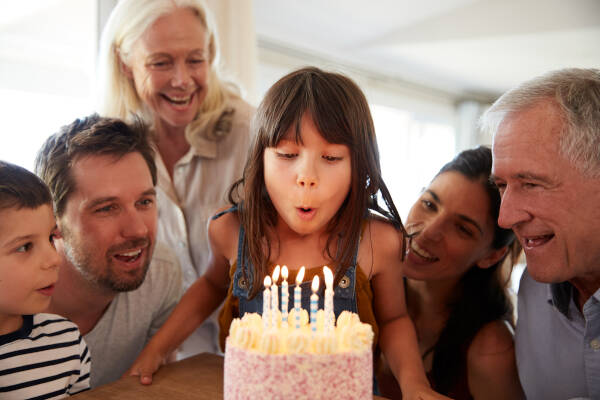 Family gathering around a young girl blowing out candles on her birthday cake, smiling and celebrating together.