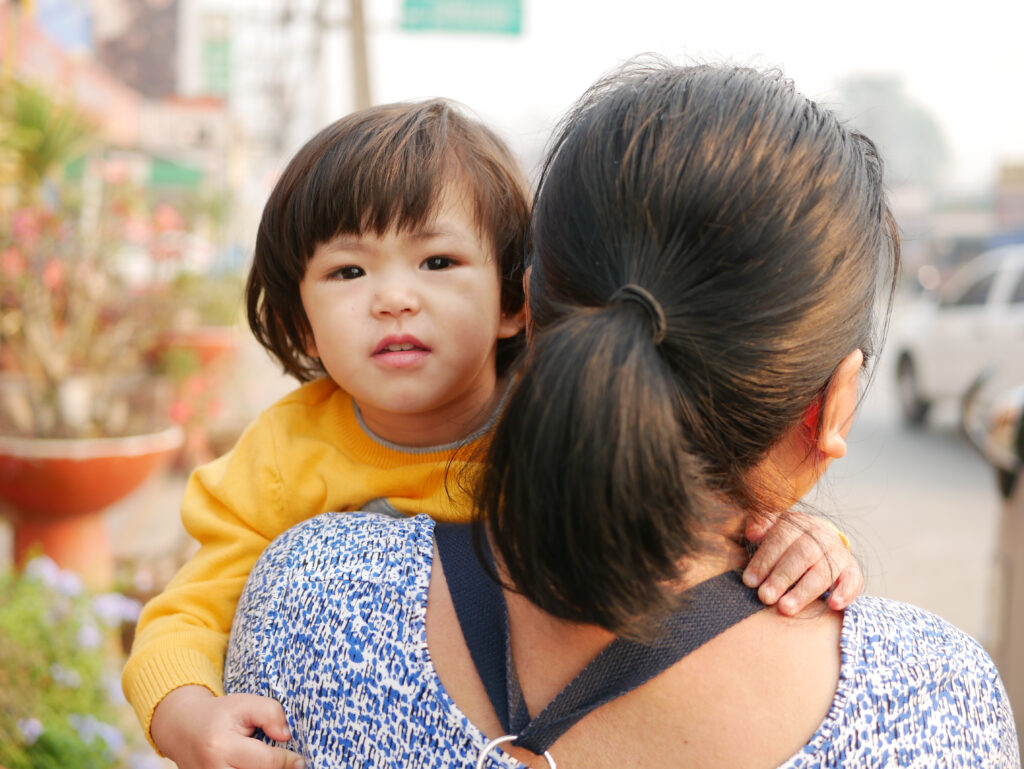 Focused shot of a two-year-old girl being carried by her auntie along the roadside.