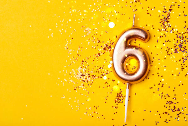 Golden number six birthday candle on a yellow background with scattered gold and white confetti.