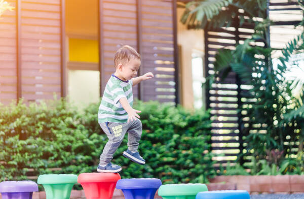 Little happy toddler boy walking on a colorful balance toy in the playground at kindergarten school.