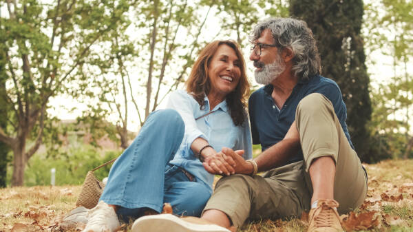 Middle-aged couple sitting together on the grass, smiling and holding hands in a peaceful outdoor setting.