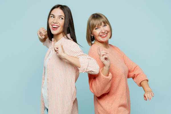 Mother and 22-year-old daughter dancing and smiling against a light blue background.