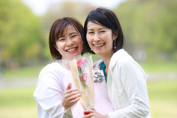 Mother and daughter share a heartfelt moment outdoors on Mother's Day, with the mother holding her gift and a bouquet of flowers.