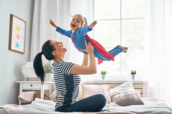 Mother and her child playing together, with the little girl in a superhero costume being helped to fly by her mother.