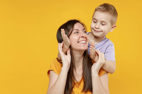 Mother and young boy playing together and laughing against a bright yellow background.