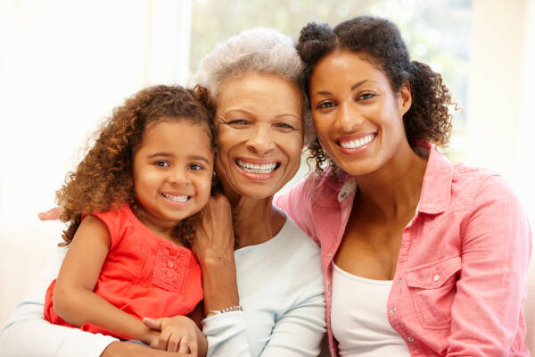 Mother, daughter, and granddaughter at home, three generations smiling at the camera.