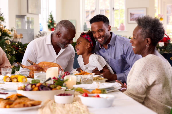 Multigenerational family sharing laughter during a holiday meal, with a young girl sitting between her father and grandfather.