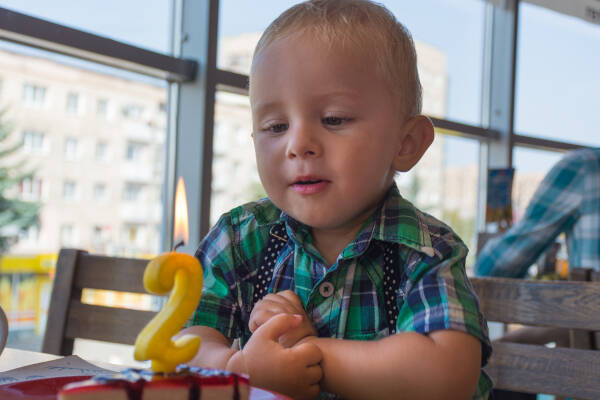 Two-year-old boy stares at a number 2 candle on a cake in a restaurant.