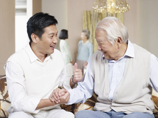 father and adult son chatting on couch.