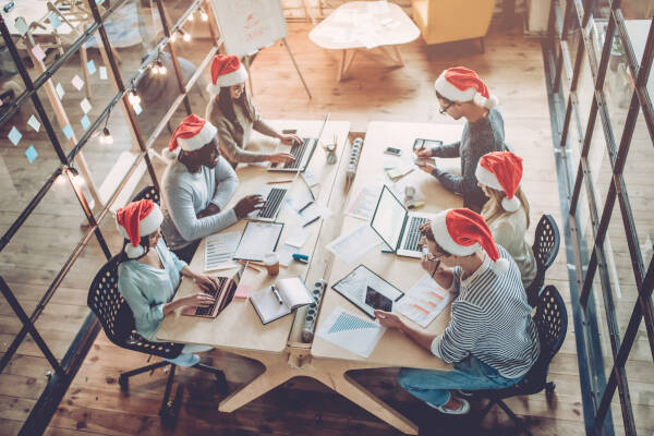 Busy office environment with employees in Santa hats working and collaborating on laptops, creating a festive and productive holiday vibe.