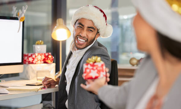 Happy coworkers in Santa hats exchanging gifts in a festive office setting, spreading holiday cheer and smiles.