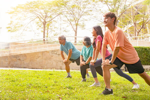 Four individuals of diverse ages stretching together in a park, smiling while enjoying an outdoor exercise session.