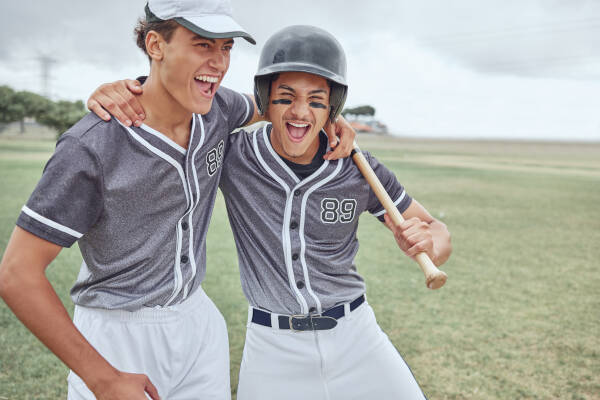 Two baseball players in matching uniforms celebrating together on a grassy field, with one holding a bat.