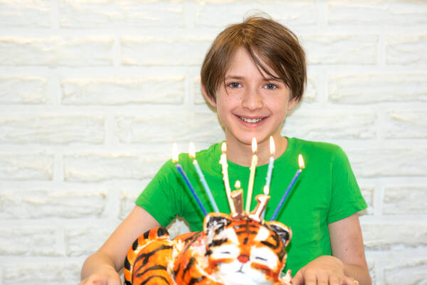 Boy in green shirt with tiger cake and candles, smiling at a birthday celebration.
