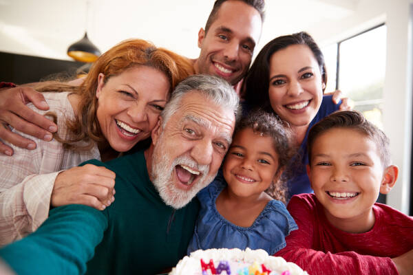 Happy family taking a selfie with an elderly man in front of a birthday cake.
