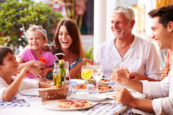 Smiling family enjoying pizza and drinks together at an outdoor restaurant.